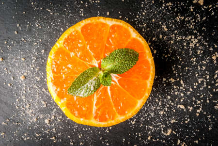 Fresh sliced ??tangerine with leaf mint and cane sugar on a black background, top view, copy space
