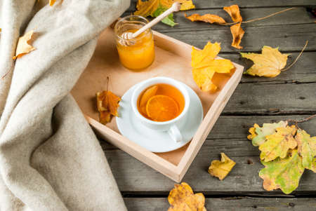 Cozy autumnal mood, warm autumn. A cup of hot tea with lemon and ginger on a rustic table, plaid,...