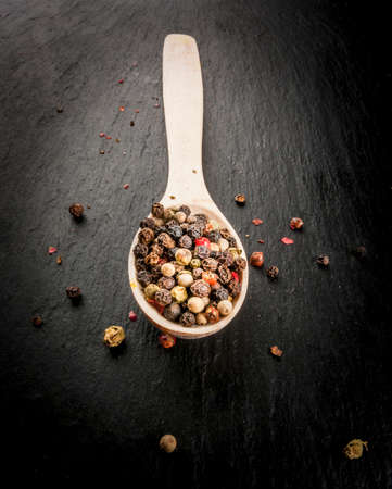 Selection of fragrant pepper - red, black and white - in a wooden spoon on a black table