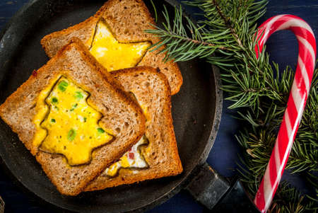 Funny food for kids, Christmas breakfast: toast with scrambled eggs in the shape of Christmas trees and stars, on dark blue festive table with fir branches and decorations, top viewの写真素材