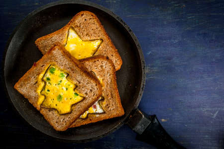 Funny food for kids, Christmas breakfast: toast with scrambled eggs in the shape of Christmas trees and stars, on dark blue festive table, top view, copy spaceの写真素材