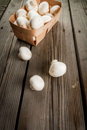 Raw mushrooms champignon in a basket on a rustic wooden table, copy spaceの写真素材