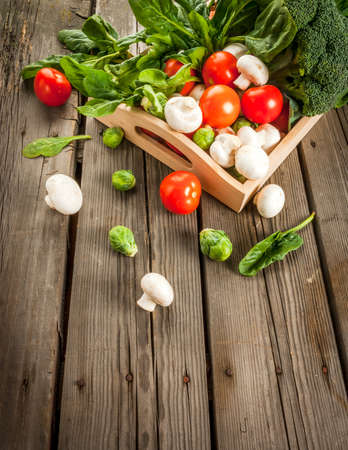 Fresh raw organic vegetables on a rustic wooden table in basket: spinach, broccoli, Brussels sprouts, tomatoes, mushrooms, champignons.の写真素材
