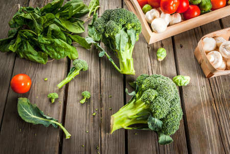 Fresh raw organic vegetables on a rustic wooden table in basket: spinach, broccoli, Brussels...