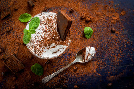 Traditional Italian dessert tiramisu decorated with cocoa and mint leaves. On a dark blue wooden table, decorated with cocoa, dark chocolate, coffee beans and mint leaves. Copy space, top viewの写真素材
