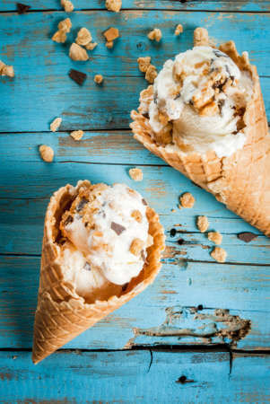 Two ice cream cones with sprinkles of chocolate and cookies on a bright blue wooden table. Summer,...