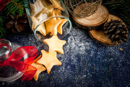 Traditional Christmas gingerbread cookies in the jar on the background of Christmas tree branches, pine cones and decoration. On a dark blue wooden table, sprinkled with powdered sugar or artificial snow. Copy spaceの写真素材