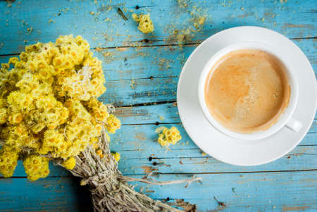 Ð¡offee mug with a bouquet of dried wildflowers and a notebook for notes and pencil. On a blue wooden table, top view, copy spaceの写真素材