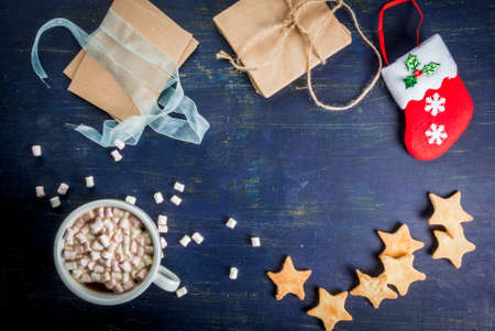 Christmas background: dark blue wooden table with traditional ginger cookies, socks for gifts, a cup of hot chocolate with marshmallows and gifts, copy spaceの写真素材