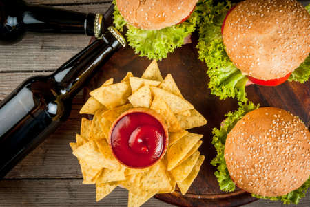 Selection of different food for a party: chips, nachos with sauces (tomato, cheese and mayonnaise tartar), burgers and beer, copy space, top viewの写真素材