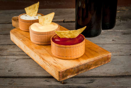 Snack for party, chips, nachos with sauces: tomato (ketchup), cheese and mayonnaise (tartar) and...