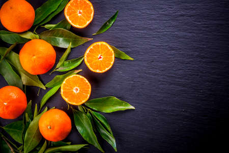Fresh tangerines with leaves on black stone background. Top view, copy spaceの写真素材