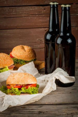 Freshly prepared homemade burger: a bun with sesame seeds, meat, cheese, lettuce, tomato and cheese sauce with beer, copy spaceの写真素材