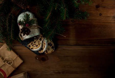 Traditional Christmas Baking: Stollen with dried fruits and nuts, sprinkled with powdered sugar. Miniature Christmas cake. Against Christmas tree branches, cones and gifts Top view copy spaceの写真素材