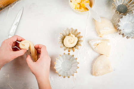 Cooking fashionable baking - scones cruffins (puffmaffin), a mixture of a croissant and a muffin.  Girl twists the roll of dough into a bun, hands in the shotの写真素材
