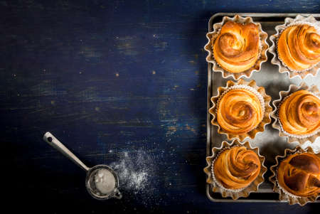 Modern fashionable pastries - scones cruffins  (puffmaffin), a mixture of a croissant and maffin. On blue dark wooden table, sprinkled with powdered sugar. Copy space, top viewの写真素材