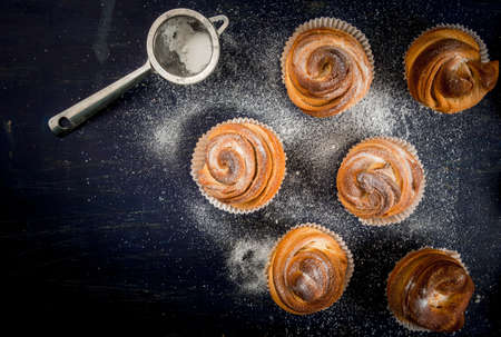 Modern fashionable pastries - scones cruffins  (puffmaffin), a mixture of a croissant and maffin. On blue dark wooden table, sprinkled with powdered sugar. Copy space, top viewの写真素材