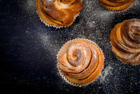 Modern fashionable pastries - scones cruffins  (puffmaffin), a mixture of a croissant and maffin. On blue dark wooden table, sprinkled with powdered sugar. Copy space, top viewの写真素材