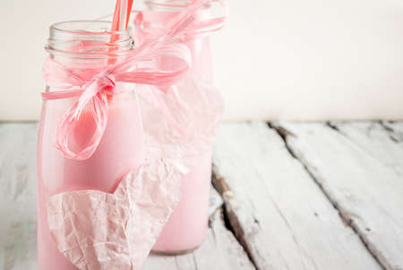 Ideas for celebrating Valentine's Day with two bottles of pink milkshake or yogurt, decorated in romantic style - ribbons and paper hearts, on white wooden table, copy space, selective focusの写真素材