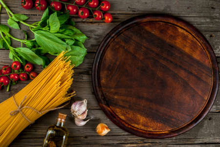Ingredients for making pasta on a wooden table: spaghetti, fresh cherry tomatoes, basil leaves, garlic, onions, flavored oil, top view, copy spaceの写真素材