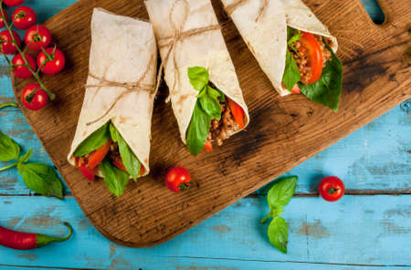 Healthy lunch snack. Sandwiches twisted roll Tortilla with beef and vegetables a wooden cutting board on blue wooden rustic table, copy space, top viewの写真素材