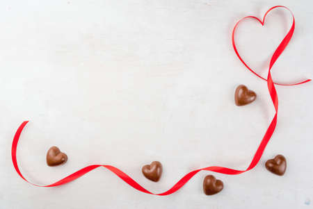 Background valentines day. White wooden table with a red ribbon in the form of hearts and candy in...