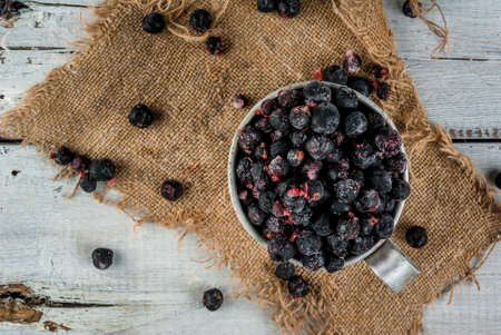 Rustic old mug with frozen blueberries and currants, on white wooden table, top view