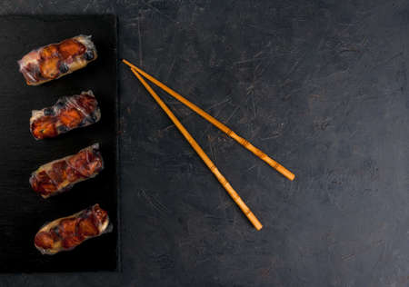 Sweet spring rolls with fruits and berries on the black stone table, next to chopsticks for sushi, top view, copy spaceの写真素材