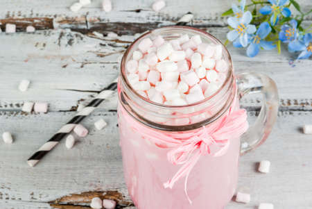 Pink hot chocolate with marshmallow, - with flowers and jar with marshmallows in the background. Spring mood. On an old white wooden table.の写真素材
