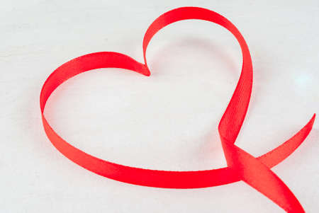 Valentine's day background. Red ribbon, lined in shape of heart on a white tableの写真素材