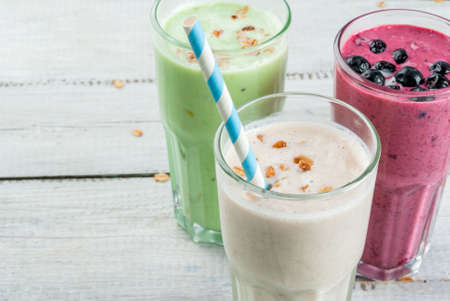 Refreshing milkshakes or smoothies: White (banana), green (apple and kiwi) and berries. On a white wooden table, close view, copy spaceの写真素材