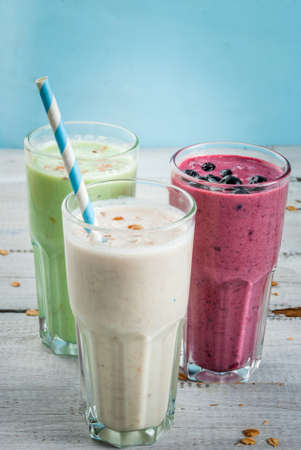 Refreshing milkshakes or smoothies: White (banana), green (apple and kiwi) and berries. On a white wooden table, copy spaceの写真素材