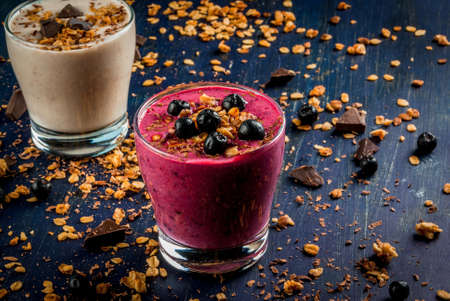 Easy and light healthy dessert of yogurt, fruit smoothies, granola and dark chocolate on a dark blue table, sprinkle dessert ingredientsの写真素材