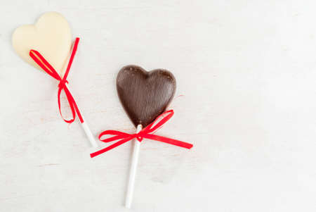 Valentine's Day background: white wooden table with candy in the form of hearts on a stick, with...