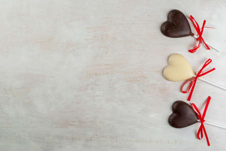 Valentine's Day background: white wooden table with candy in the form of hearts on a stick, with festive red ribbons, top view, copy spaceの写真素材