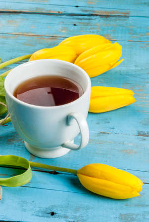 Spring flowers tulips and cup of tea on a light blue rustic wooden table, copy space, verticalの写真素材