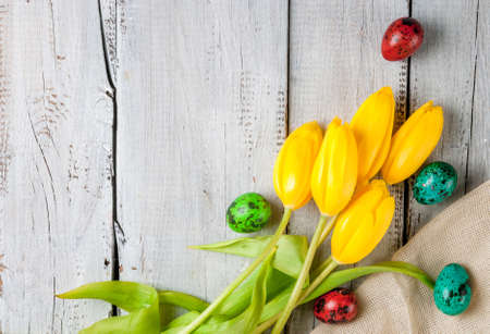Spring Holiday Easter: colored eggs and flowers tulips on the wooden table, copy space, top viewの写真素材