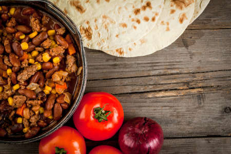 Traditional Mexican and Chilean dish of chilli con carne. In the rustic pan, next to tortillas and fresh vegetables on a wooden table, copy spaceの写真素材
