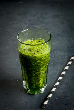 Healthy diet, green smoothies, vegetables and herbs (basil, parsley, spinach). On a dark stone table, with a straw to drink, copy spaceの写真素材