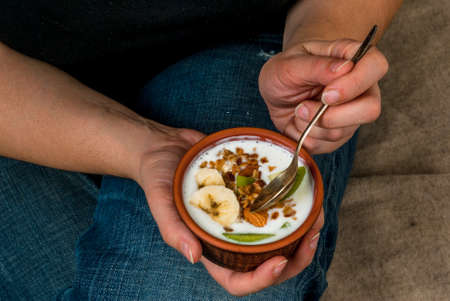 iet concept. Plus size (fat) girl eating diet and healthy breakfast: homemade yogurt with golden granola with nuts and fresh fruit (kiwi and banana)の写真素材