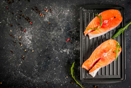 Raw uncooked salmon steaks on the boards for the grill, on a dark gray stone kitchen table. With salt, spices, seasonings, herbs and vegetables for cooking.  Top view, copy spaceの写真素材