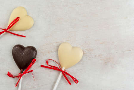 Valentine's Day background: white wooden table with candy in the form of hearts on a stick, with festive red ribbons, top view, copy spaceの写真素材