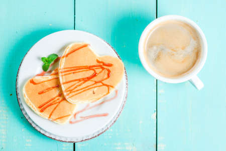 Breakfast on Valentine's Day: Pancake in the form of hearts with red cherry sauce, a cup of coffee. On a light blue wooden table, top view, copy spaceの写真素材