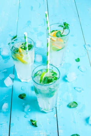 Selection of summer refreshing cocktails with mint (lemonade or mojito): with lemon, orange, lime. On light blue wooden table, bright sunlight. Copy space, close viewの写真素材