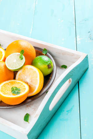 Tray with whole and cut citrus (orange, lemon, lime), decorated with mint leaves. On a blue wooden table, copy spaceの写真素材