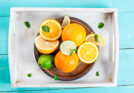 Tray with whole and cut citrus (orange, lemon, lime), decorated with mint leaves. On a blue wooden table, top view, copy spaceの写真素材