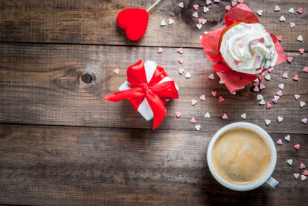 St. Valentine's Day. Coffee, cake with cream and sugar sprinkles (hearts), gift and decoration in form of heart are on table.Top view, copy spaceの写真素材