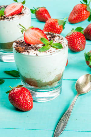 Summer dessert, classic cheesecake with strawberries decorated with mint leaves. On a light blue wooden table, bright sunlight.の写真素材
