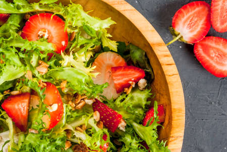 Summer salad with strawberries and greens (spinach, lettuce), in a wooden bowl on a dark gray stone (concrete) table, top close view, copy spaceの写真素材
