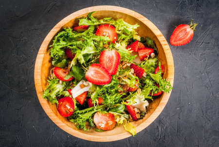 Summer salad with strawberries and greens (spinach, lettuce), in a wooden bowl on a dark gray stone (concrete) table, top view, copy spaceの写真素材